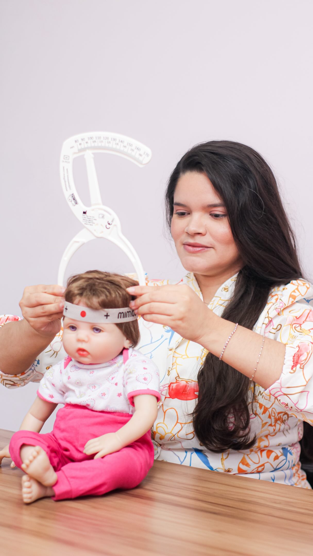 Gleiciane observa uma boneca e demonstra uma medição da cabeça no consultório