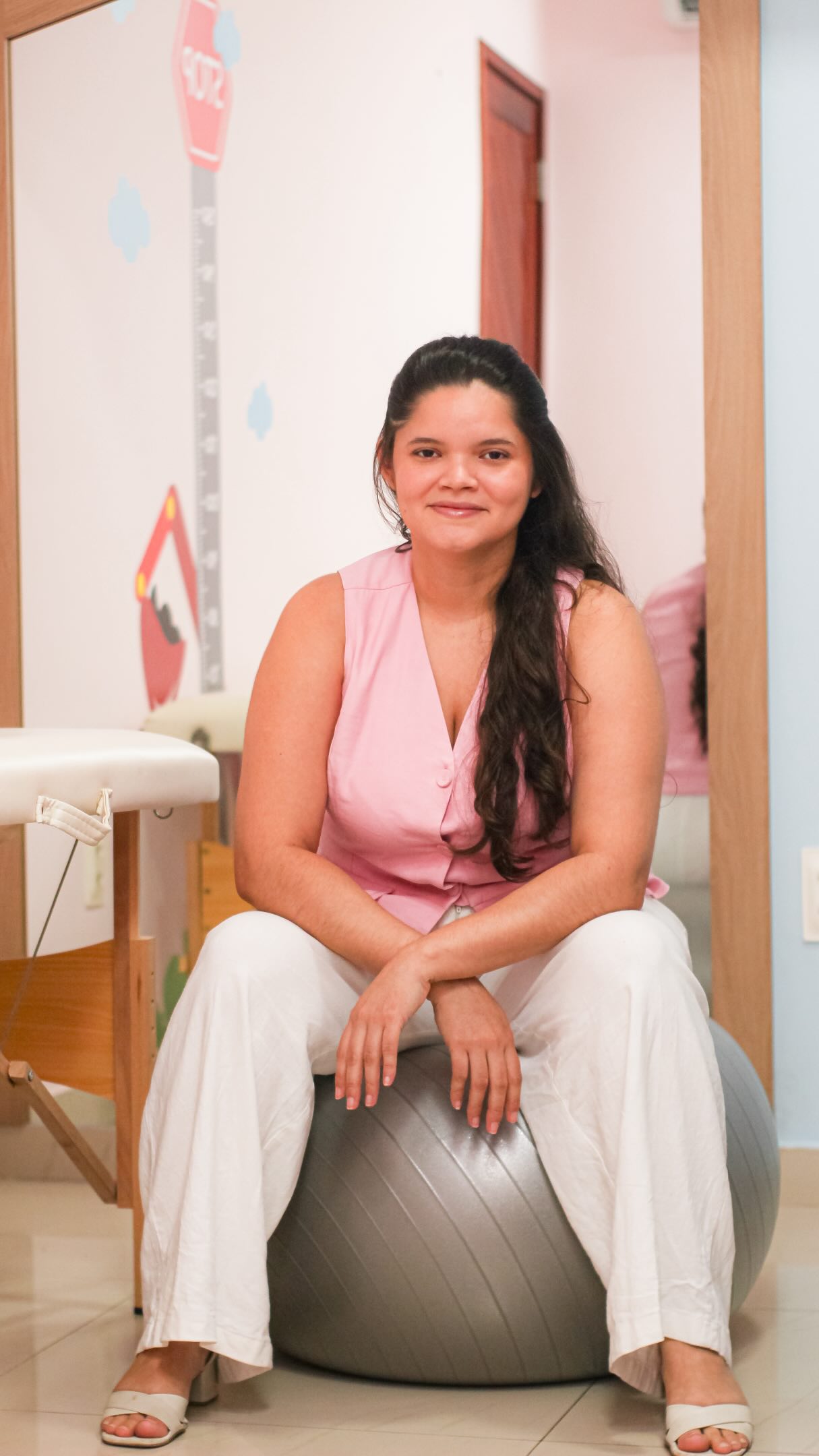 Retrato de Gleiciane sentada no consultório com blusa rosa